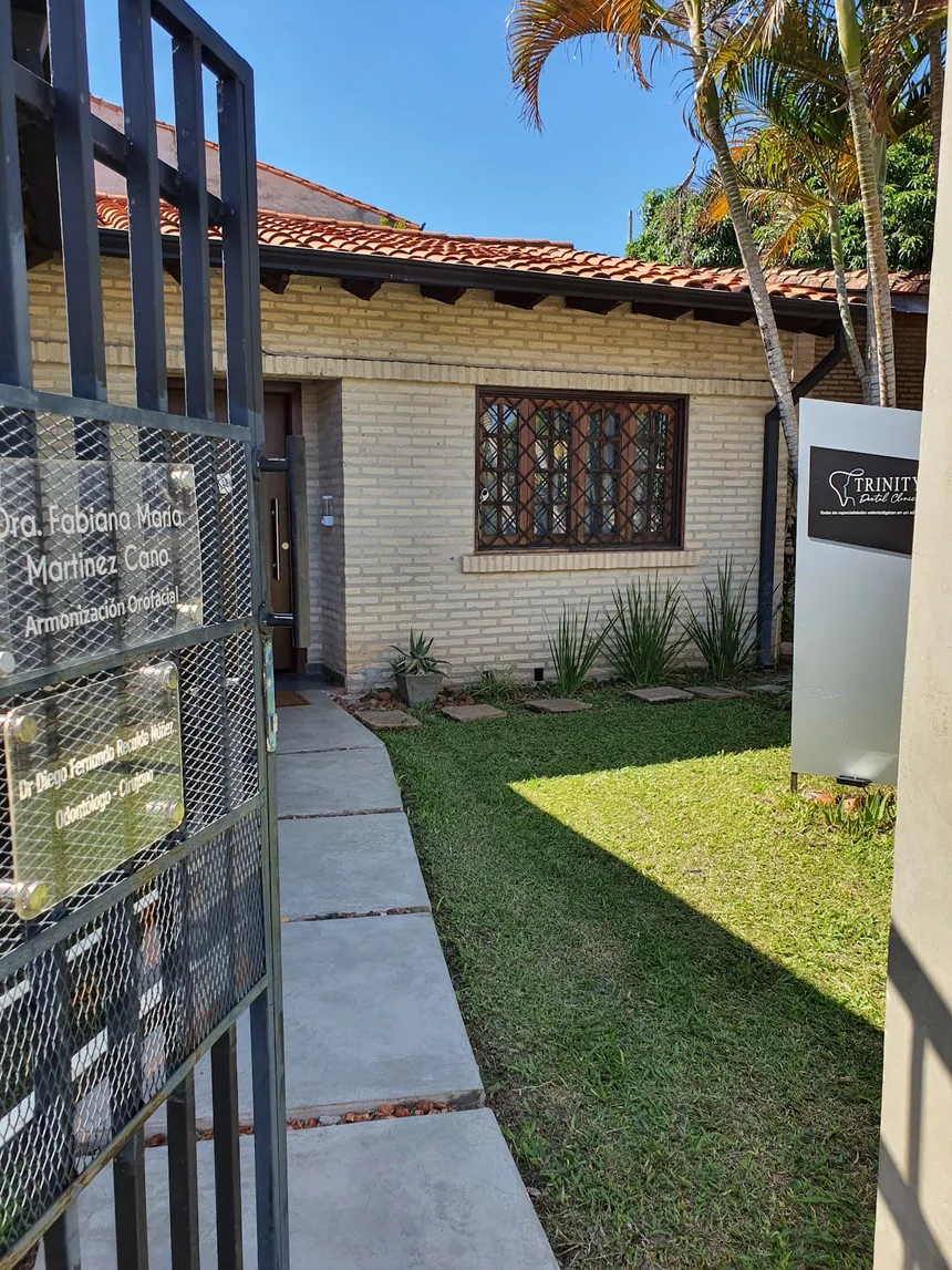 Entrada de Trinity Dental Clinic en Luque, con el tótem de la clínica sobre el jardín